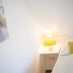 Schlafzimmer mit Bett, Nachttisch und Lampe. Wandbild zeigt Strand.