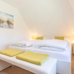 Schlafzimmer mit Doppelbett, gelben Kissen und Handtüchern, Wandbild und Nachttischen.