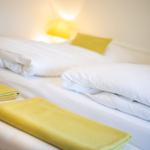 Ein Bett mit weißen Laken und zwei gelben Kissen. Zwei gelbe Handtücher liegen auf dem Bett.