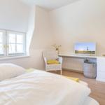 Schlafzimmer mit Bett, Fenster, Stuhl und Fernseher an der Wand.