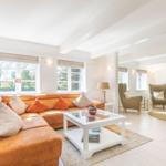Wohnzimmer mit orangefarbenem Sofa, Glas-Tisch und zwei Sesseln.