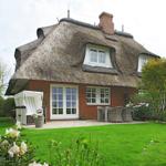 House with thatched roof, terrace, and garden with seating.