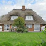 House with thatched roof, white-framed windows, and garden with seating.