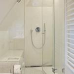 Dusche mit Glaswand und Duschbrause, daneben Heizung und Toilettenpapier.