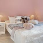 Schlafzimmer mit Bett, Nachttisch und Lampen an rosa Wänden.