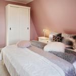 Schlafzimmer mit Bett, Schrank und Nachttisch. Wände rosa, Boden hell.