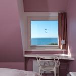 Ein Fenster mit Meerblick, Schreibtisch und Stuhl in einem Raum mit rosa Wänden.