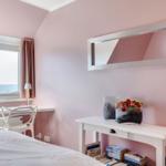 Schlafzimmer mit Blick aufs Meer, rosa Wände, Spiegel und Schreibtisch.