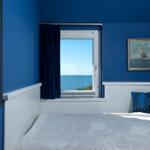 Schlafzimmer mit Blick auf das Meer, blaue Wände und weißer Paneelenverkleidung.