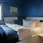 Schlafzimmer mit blauer Wand, Bett mit Kissen und Nachttisch mit Lampe.