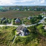 Dorf mit strohgedeckten Häusern und grünen Hängen. Blick aufs Meer.