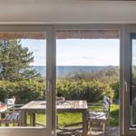 Durch die Glastüren blickt man auf einen Garten mit Tisch und Stühlen. Im Hintergrund ist das Meer zu sehen.
