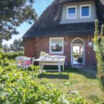 Haus mit Strohdach, weißer Tisch und Stühle im Garten. Tür führt ins Innere.