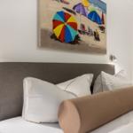 Bettkopfteil mit Kissen und Wandbild mit Strandmotiv.