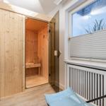 Sauna mit Holzwand und Sitzbank, daneben Fenster mit Jalousie und Liegestuhl.