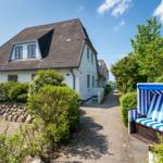Weiße Ferienhaus mit Dachgaube und blau-weißem Strandkorb.