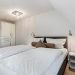 Schlafzimmer mit Doppelbett, weißen Wänden und moderner Beleuchtung.