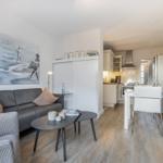 Wohn- und Essbereich mit Küche. Sofa, Tisch und Stühle sind sichtbar.