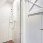 Dusche mit Duschbrause und weißen Fliesen. Tür mit Metallgriff.