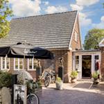 Ein Haus mit Schopf und Terrasse, auf der ein Sonnenschirm und Fahrräder stehen.