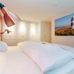 Bedroom with bed, white closets, and lamp. Wall art shows lighthouse.