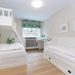 Room with loft bed, desk, and window with floral roller blind.