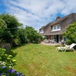 House with thatched roof, garden, lounge chair, and terrace with table and chairs.