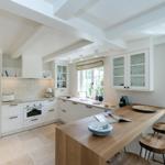 Kitchen with wooden island, white cabinets, and stone floor. Windows with view of greenery.