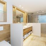 Modern bathroom with wooden shelves and mirrors. White tiles and towels.