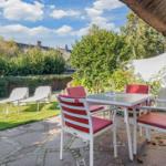 Terrasse mit Tisch, Stühlen und Liegen im Garten. Hintergrund: grüne Hecke und Himmel.