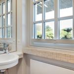 Badezimmer mit Waschbecken, Spiegel und Fensterblick auf Grünflächen.