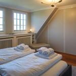 Zwei Betten mit weißen Bettwäsche und Handtüchern. Fenster, Schrank und Holzboden.