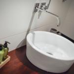 Waschbecken auf Holzunterschrank mit modernem Wasserhahn und grünen Flüssigseifenflaschen.