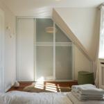 Schlafzimmer mit Dachschrägen, Kleiderschrank und Fenster.