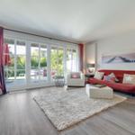 Wohnzimmer mit rotem Sofa, weißen Sesseln und Blick auf den Garten.