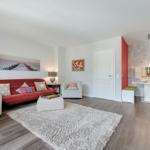 Wohnbereich mit rotem Sofa, weißem Sessel und Teppich. Küche mit Küchentisch und roten Wänden.