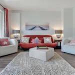 Ein Wohnzimmer mit rotem Sofa, zwei weißen Sesseln und einem flauschigen Teppich.