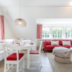 Wohn- und Essbereich mit rotem Sofa, weißem Tisch und Stühlen sowie roten Gardinen.