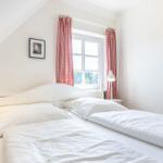 Zimmer mit Doppelbett, Fenster und roten Gardinen.