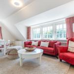 Wohn- und Essbereich mit rotem Sofa, Stuhl und Gardinen.