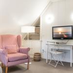 Ein Raum mit Sessel, Schreibtisch und Fernseher an der Wand.