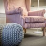 Ein Sessel mit kariertem Stoff und ein gestrickter Hocker stehen im Raum.