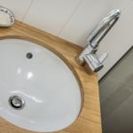 Waschbecken mit Wasserhahn auf Holzplatte, daneben Seifenschale.