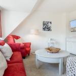 Wohnzimmer mit rotem Sofa, weißem Tisch und Fernseher an der Wand.