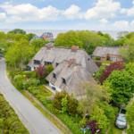 Thatched-roof house surrounded by trees and garden. View of the sea.