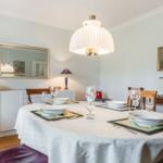 Round table set for six, illuminated by a ceiling lamp.