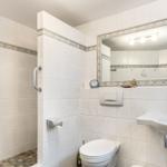 Bathroom with shower, toilet, and sink. Tiled wall with decorative border.