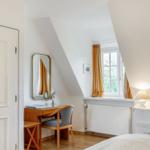 Bedroom with desk, mirror, and window with curtains.