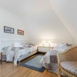 Two beds with patterned bedspreads, wooden floor, and desk in attic room.