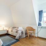 Bedroom with sloped ceiling, bed, nightstand, chair, and window.